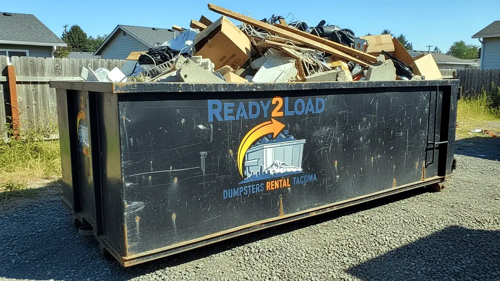 Black Ready2Load dumpster full of junk and boards in a backyard
